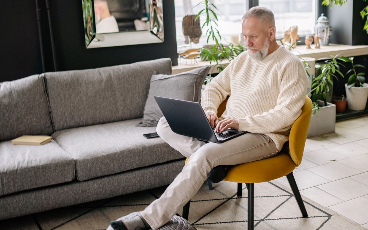 An older patient sitting at home using a laptop, the kind of person now letting an AI browser search for a doctor and book an appointment
