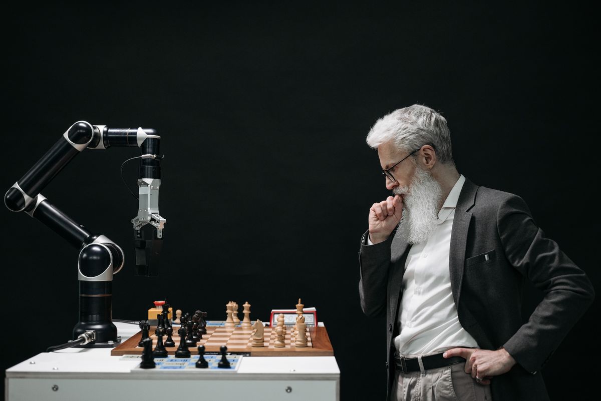 A man studying a chessboard against a robotic arm, a picture of human oversight over AI in healthcare