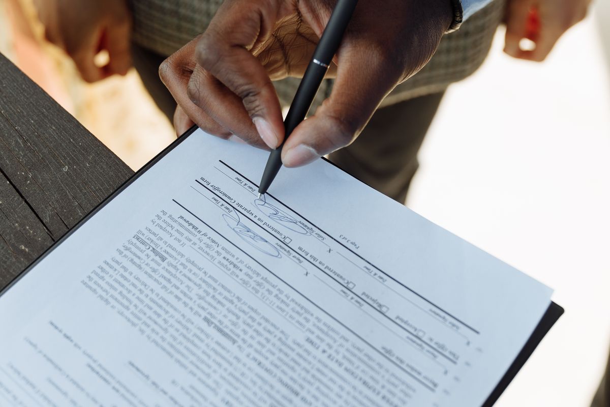 A person signing an AI vendor contract with a pen, representing a medical practice agreeing to healthcare AI terms