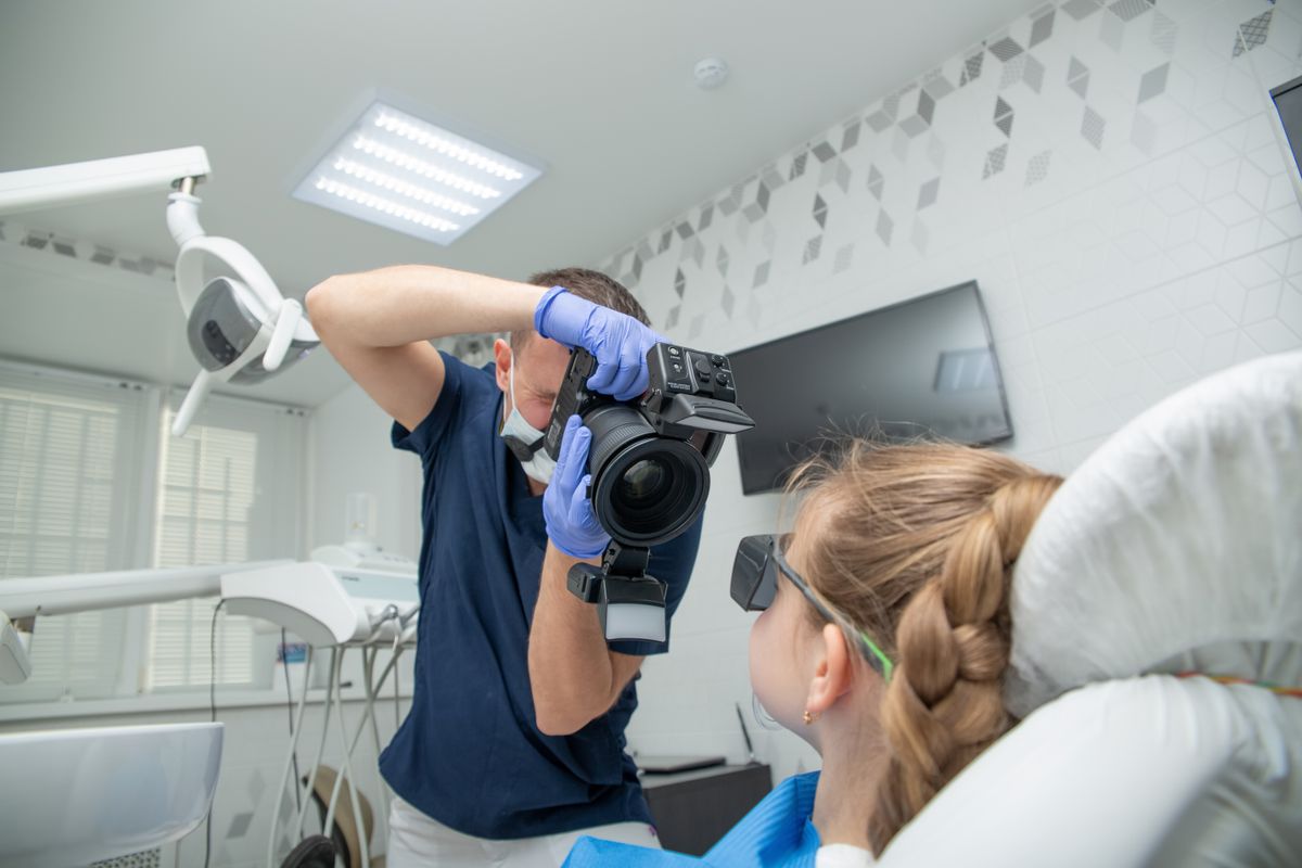 A dentist photographing a young patient's teeth during a visit, the kind of real clinic photo that can rank in image search when it is named and described