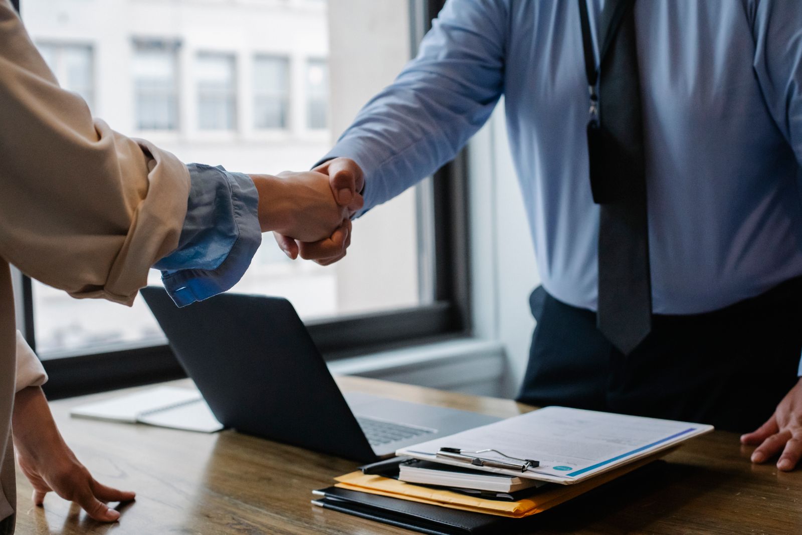 Two people shaking hands over paperwork and a laptop, the kind of referral arrangement a medical practice has to think twice about