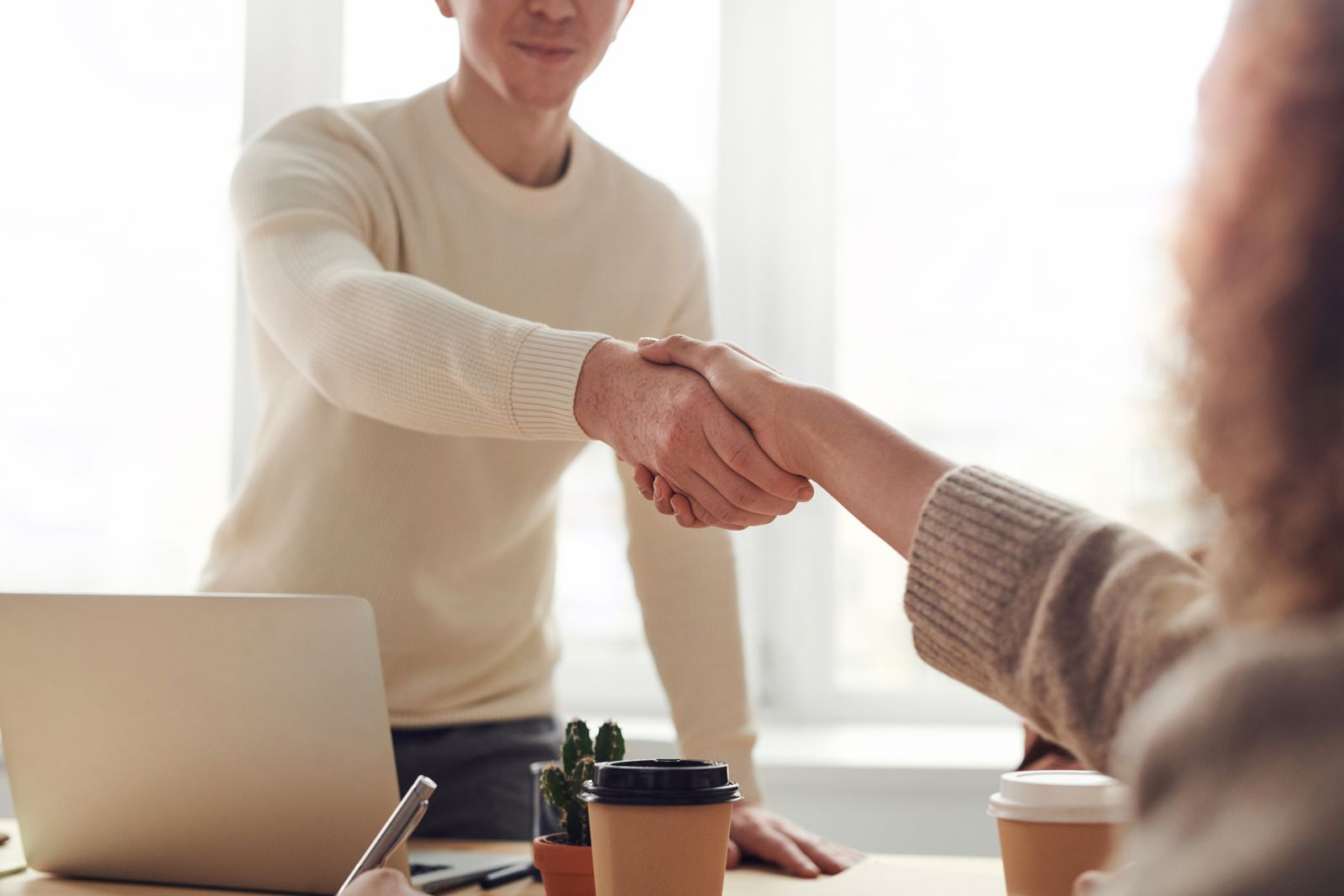 Two people shaking hands over a desk, closing a medical practice ownership change or rebrand deal