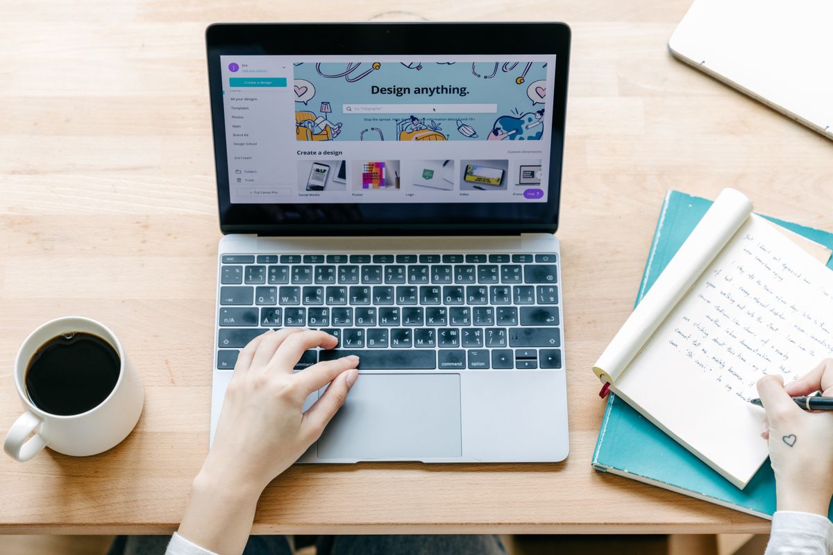 A person building an email newsletter on a laptop at a desk with coffee and a notebook, representing a medical practice creating a patient newsletter