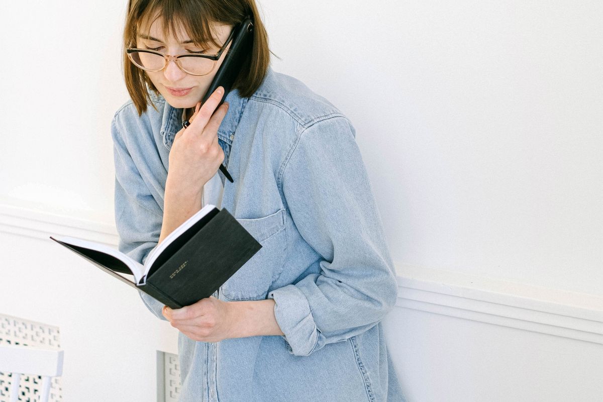 A woman at home on a phone call with notes in front of her, contacting more than one medical practice to book an appointment