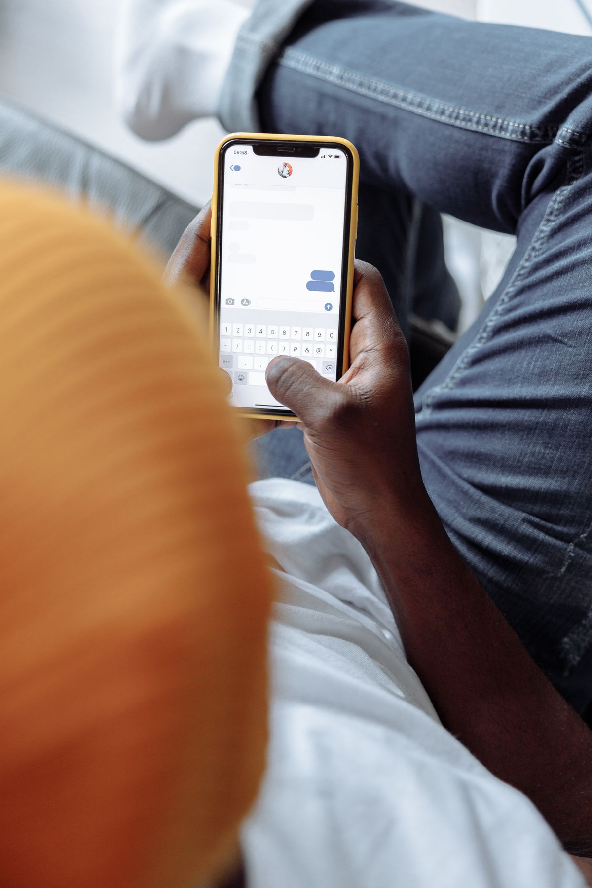 A patient sitting on a couch reading and replying to a text message on a smartphone, the way most people now prefer to hear from their doctor