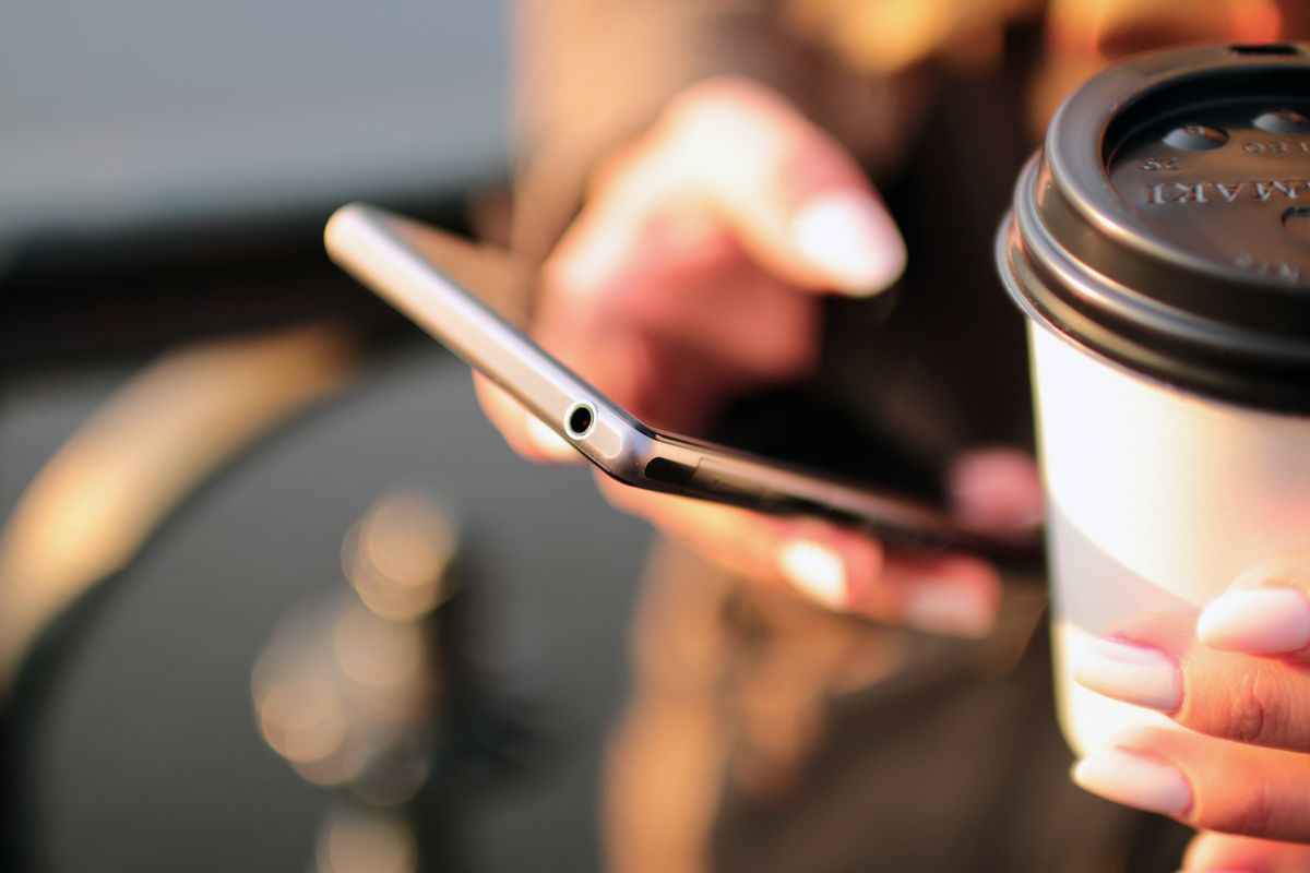 A patient texting on a smartphone while holding a coffee, representing how patients prefer to text a medical practice