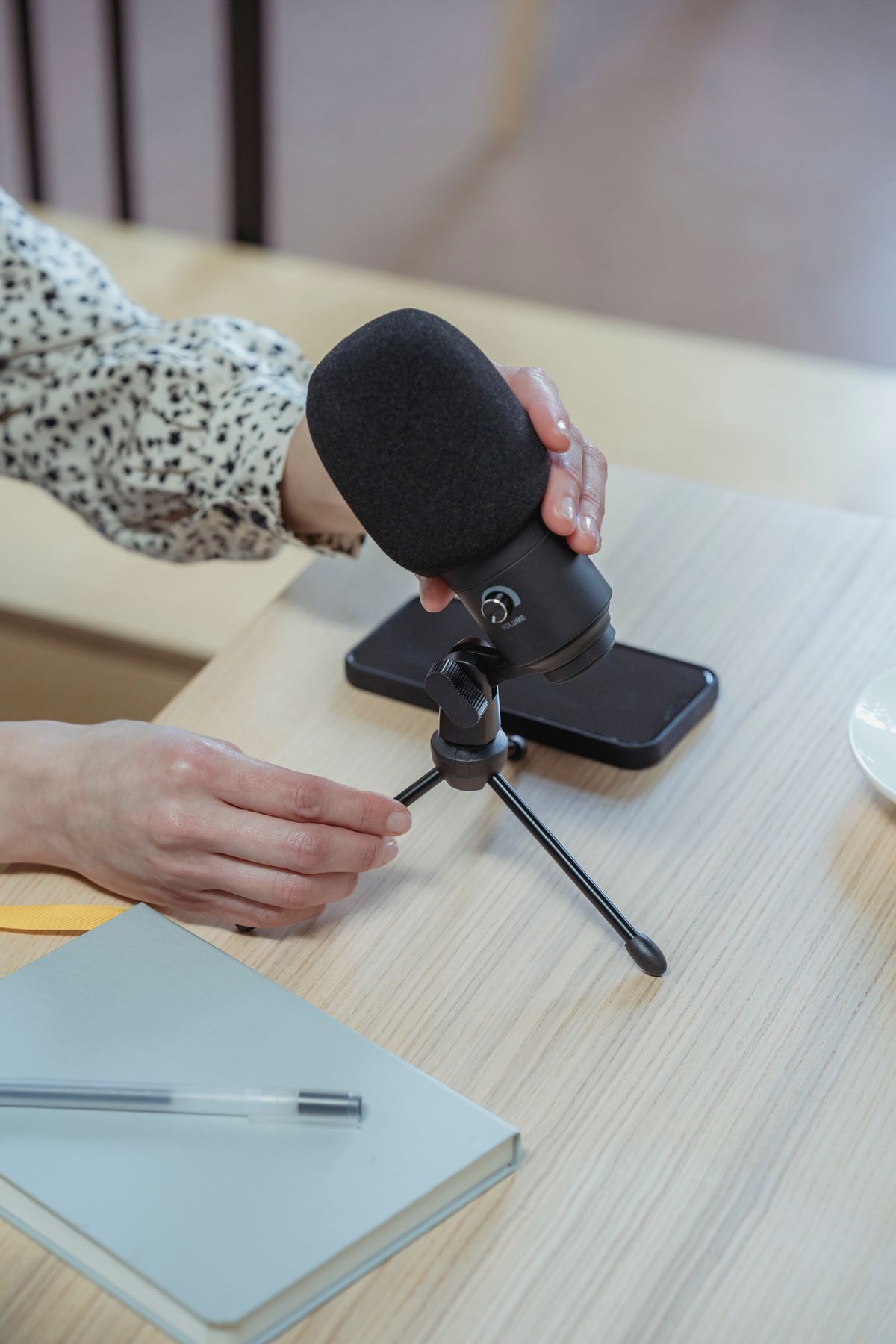 A person setting up a podcast microphone on a desk, the kind of audio recording that now carries ads a local medical practice can buy