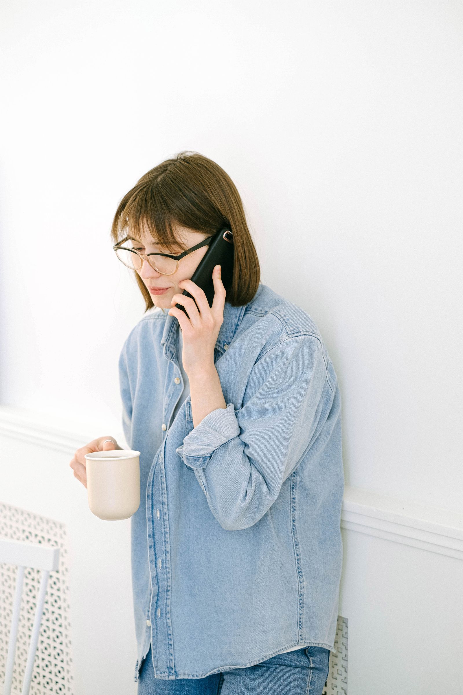 A patient tapping her phone to call a medical practice while holding a mug of coffee at home