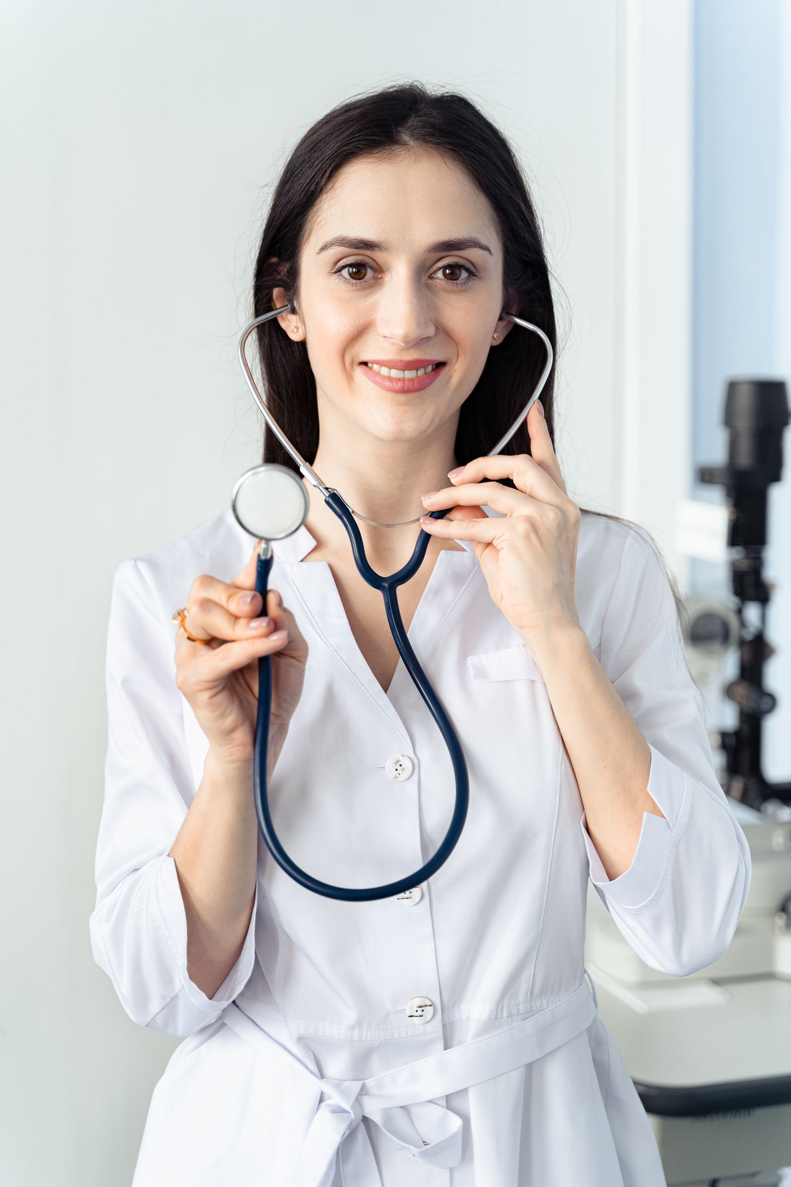 A smiling doctor in a white coat making warm eye contact with the camera, the kind of headshot that builds patient trust before a booking