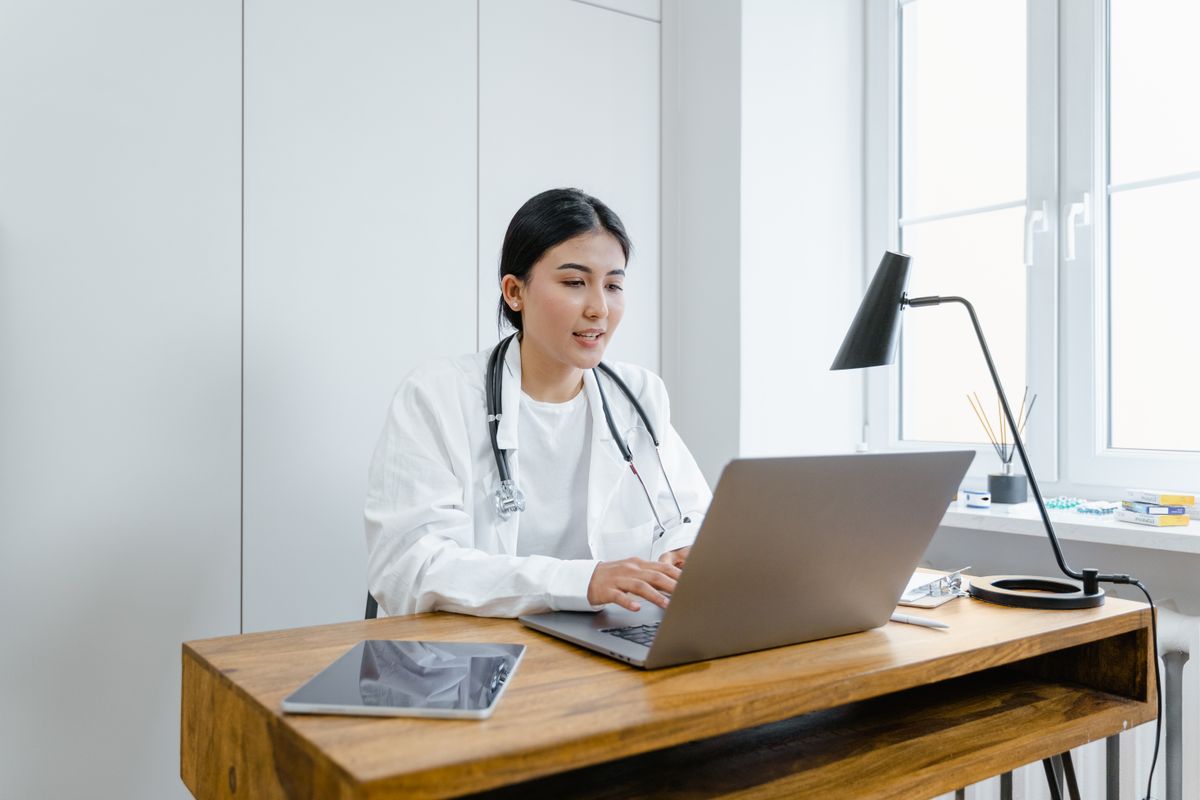 A doctor in a white coat writing medical content at a laptop, showing real clinical expertise behind a practice website