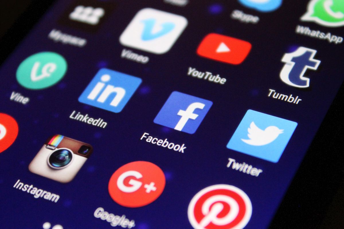 A person holding a smartphone showing a folder of social media apps, the way a patient checks a medical practice on Facebook before booking