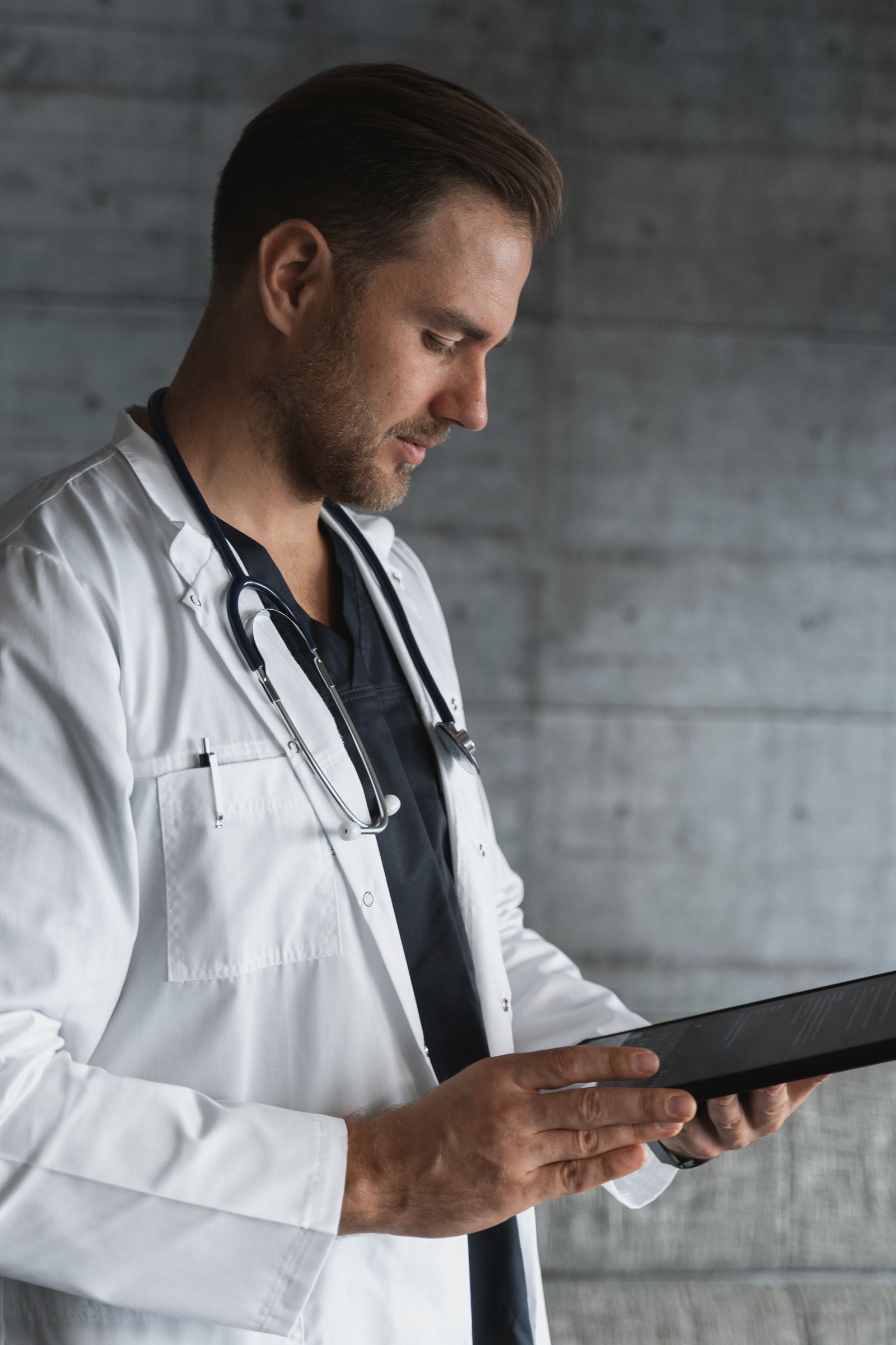 A doctor in a white coat with a stethoscope reviewing content on a tablet, representing a clinician checking medical website content before it is published