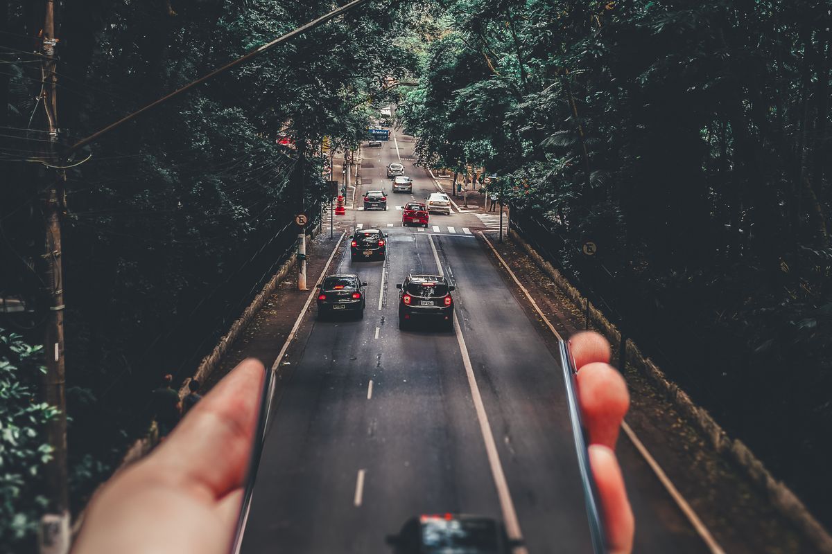 Hand holding a phone above a road full of cars, showing how patients travel to reach a higher rated medical practice