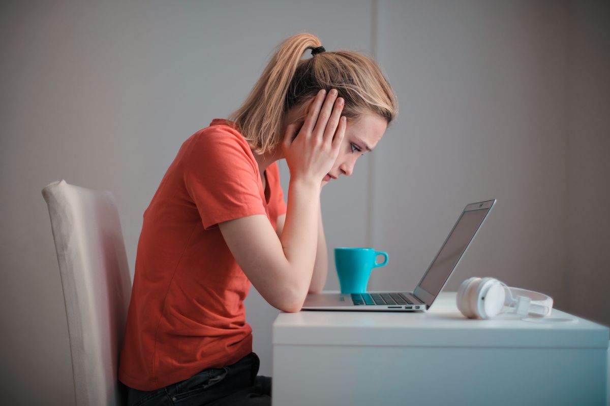 A stressed medical practice owner holding her head while reading a bad Google review from a former employee on a laptop