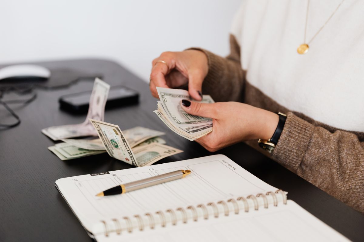 A person counting cash at a desk next to a silenced phone, representing the revenue a medical practice loses to missed patient calls