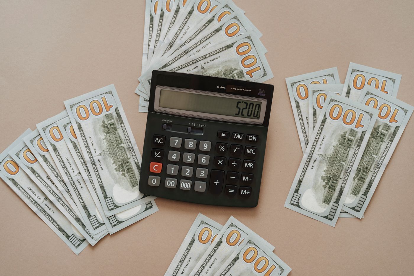 A calculator sitting on a fan of one hundred dollar bills, showing the rising cost of medical care as AI billing fights push prices up