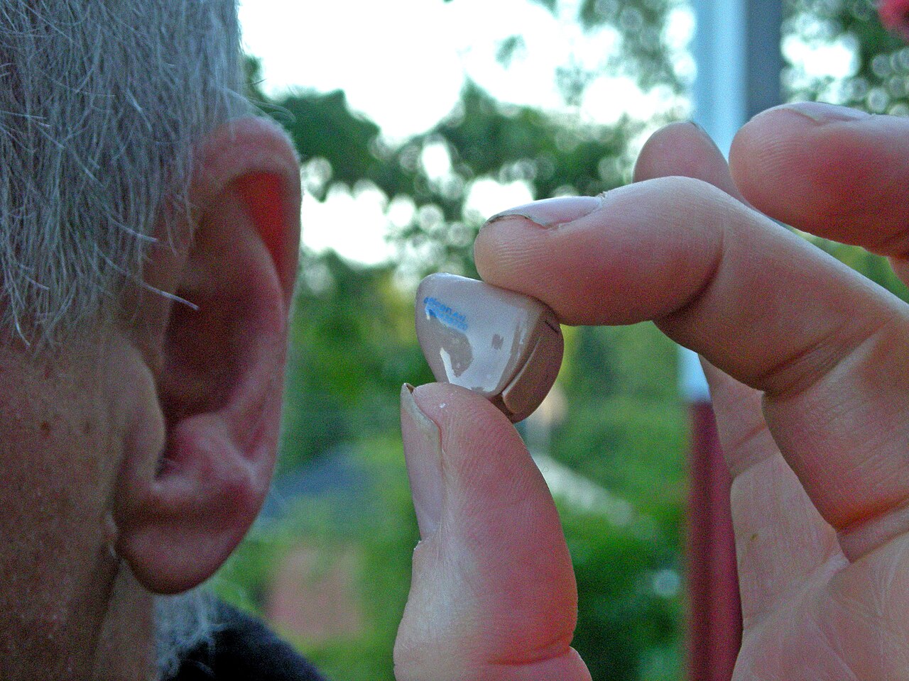 Close up of a small hearing aid held near a patient's ear