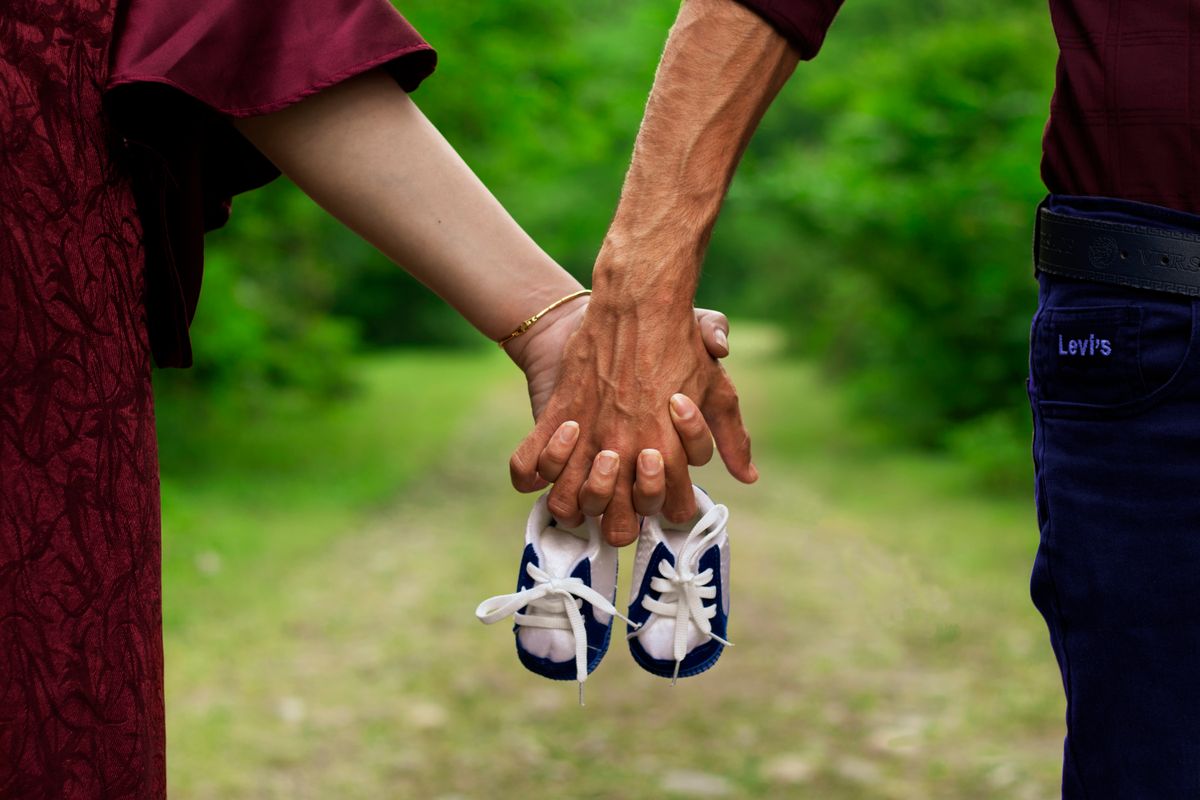A hopeful couple holding hands and holding tiny baby shoes, the kind of patients choosing a fertility clinic for their family