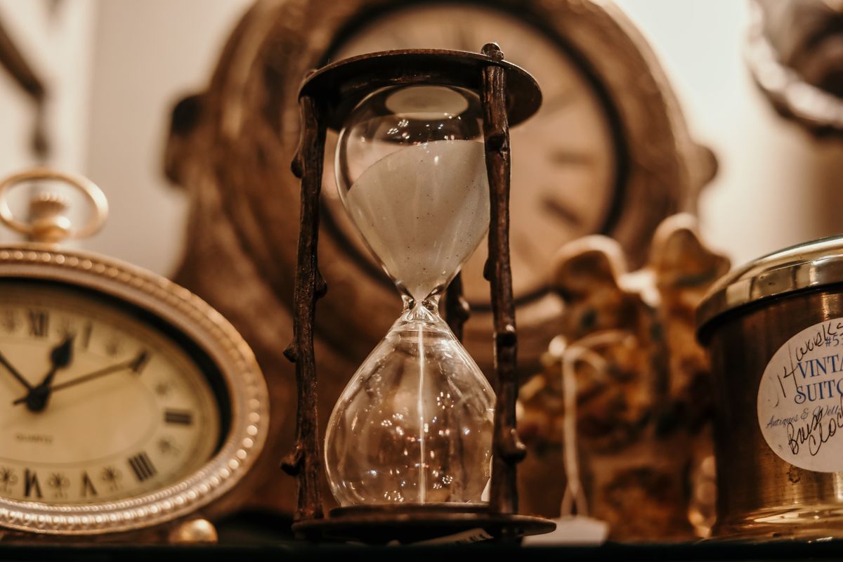 An hourglass and old clocks, the way a long appointment wait time feels to a patient who needs to be seen now
