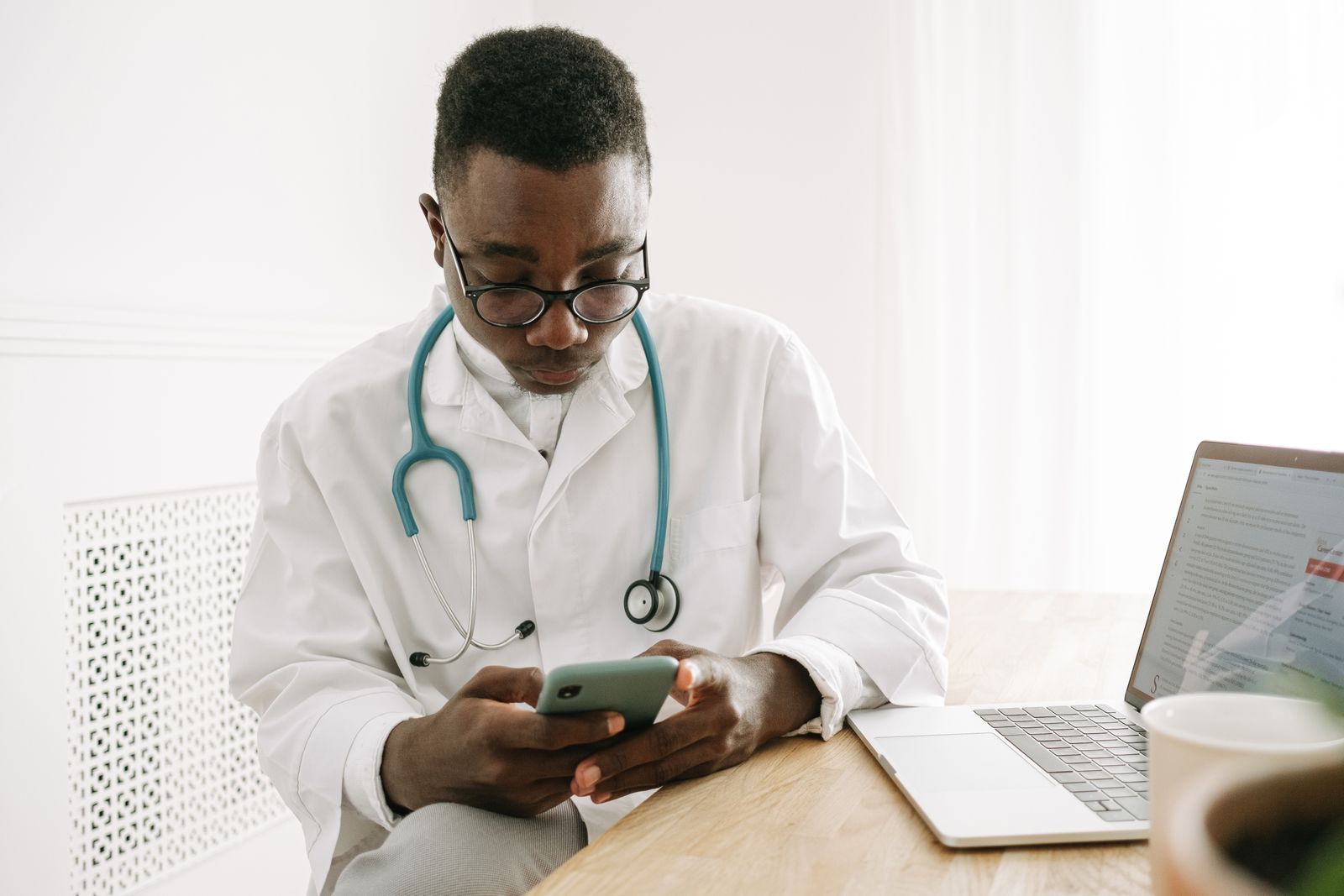 A doctor checking a smartphone at a desk, reviewing patient feedback across online review sites