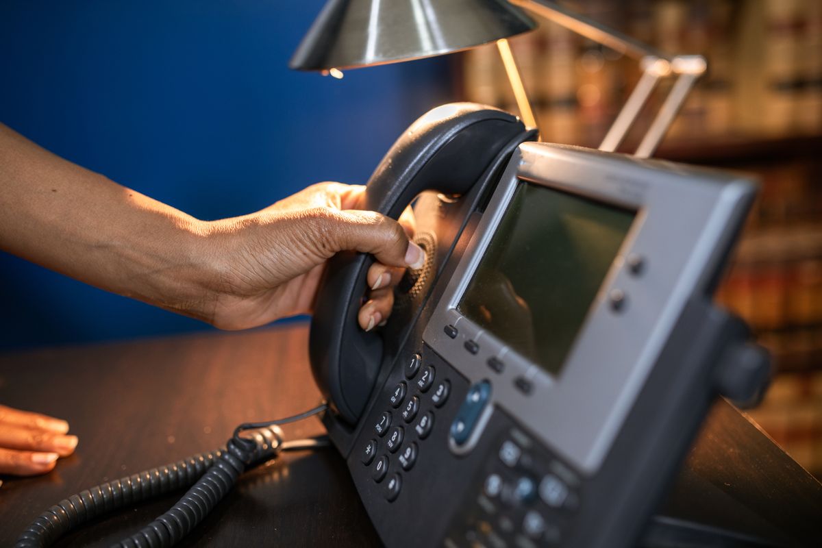 A hand reaching for an office desk phone, representing how fast a medical practice answers patient calls before they hang up