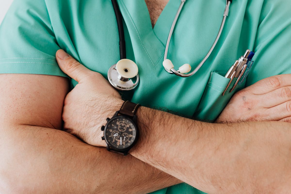 Healthcare provider in scrubs with a stethoscope and watch, standing with arms crossed, thinking about the cost of an AI receptionist for a medical practice