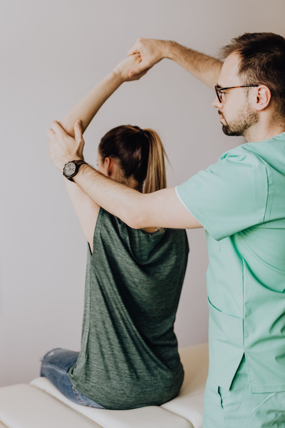 A physical therapist in scrubs guiding a patient through a shoulder stretch during a direct access physical therapy session