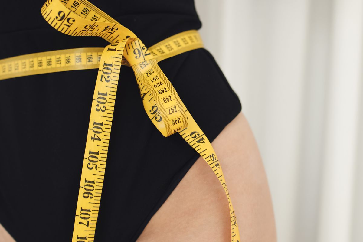 Person measuring their waist with a tape measure, representing a body contouring clinic client focused on visible results
