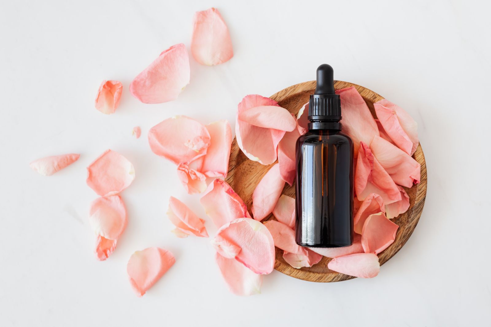Amber dropper bottle of a natural herbal remedy resting on a wooden dish surrounded by rose petals, representing naturopathic and botanical medicine