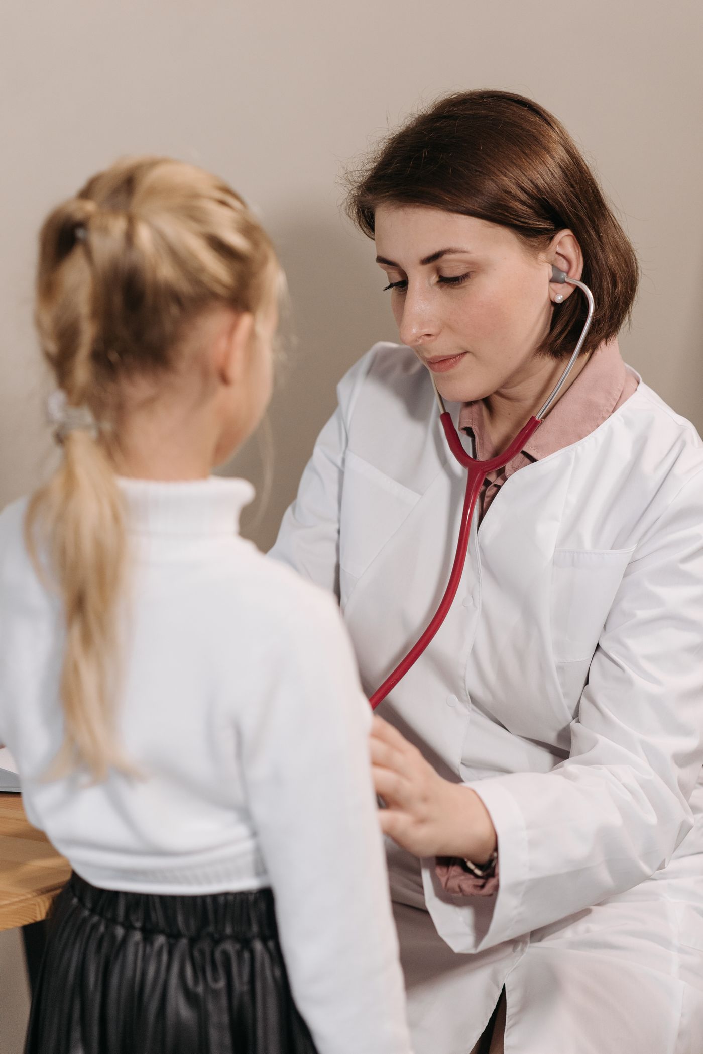 A pediatrician using a stethoscope to examine a young child during a well visit, representing the trust at the center of pediatric practice marketing