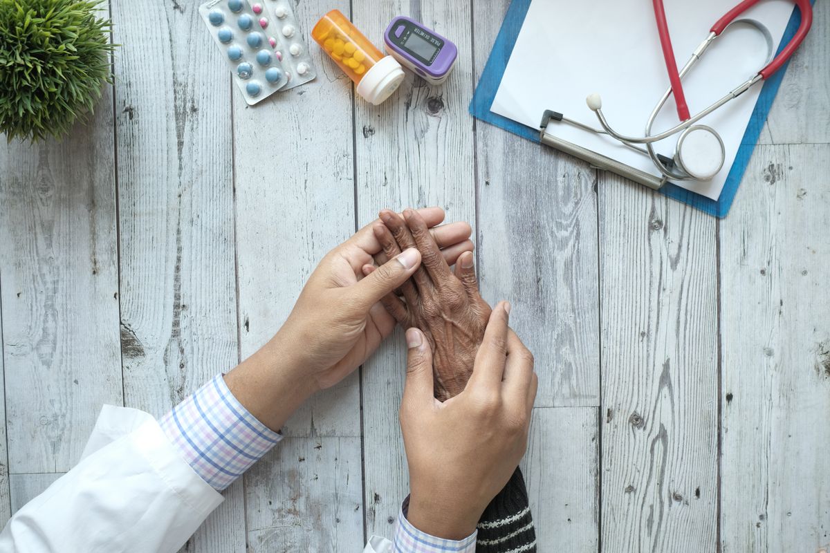 A clinician holding the hand of an older patient during a rheumatology consultation about joint pain