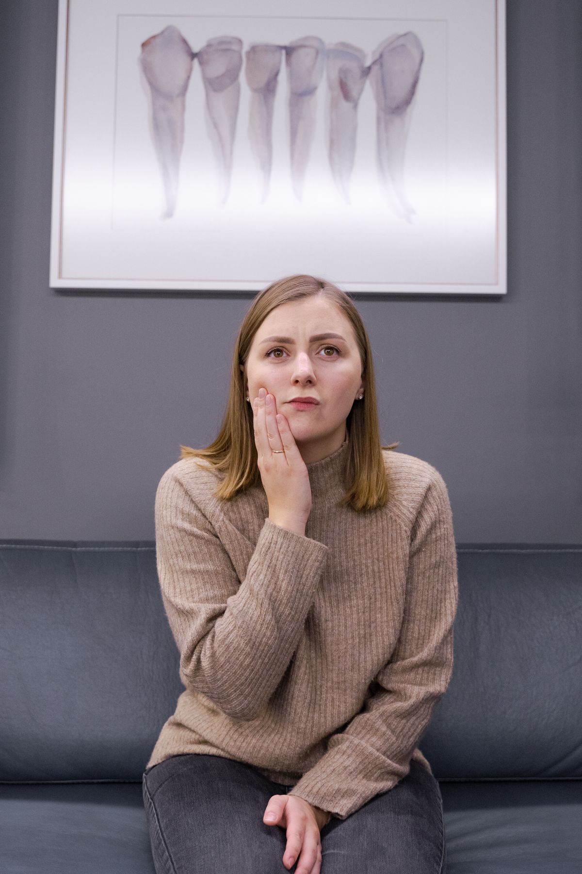 A woman holding her jaw in pain in a dental office, the kind of TMJ patient who searches for symptoms like jaw clicking and ear pain before finding a TMJ clinic
