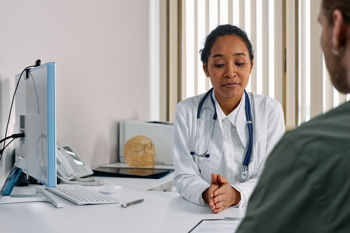 A urologist in a white coat consulting privately with a male patient across a desk in a calm exam office