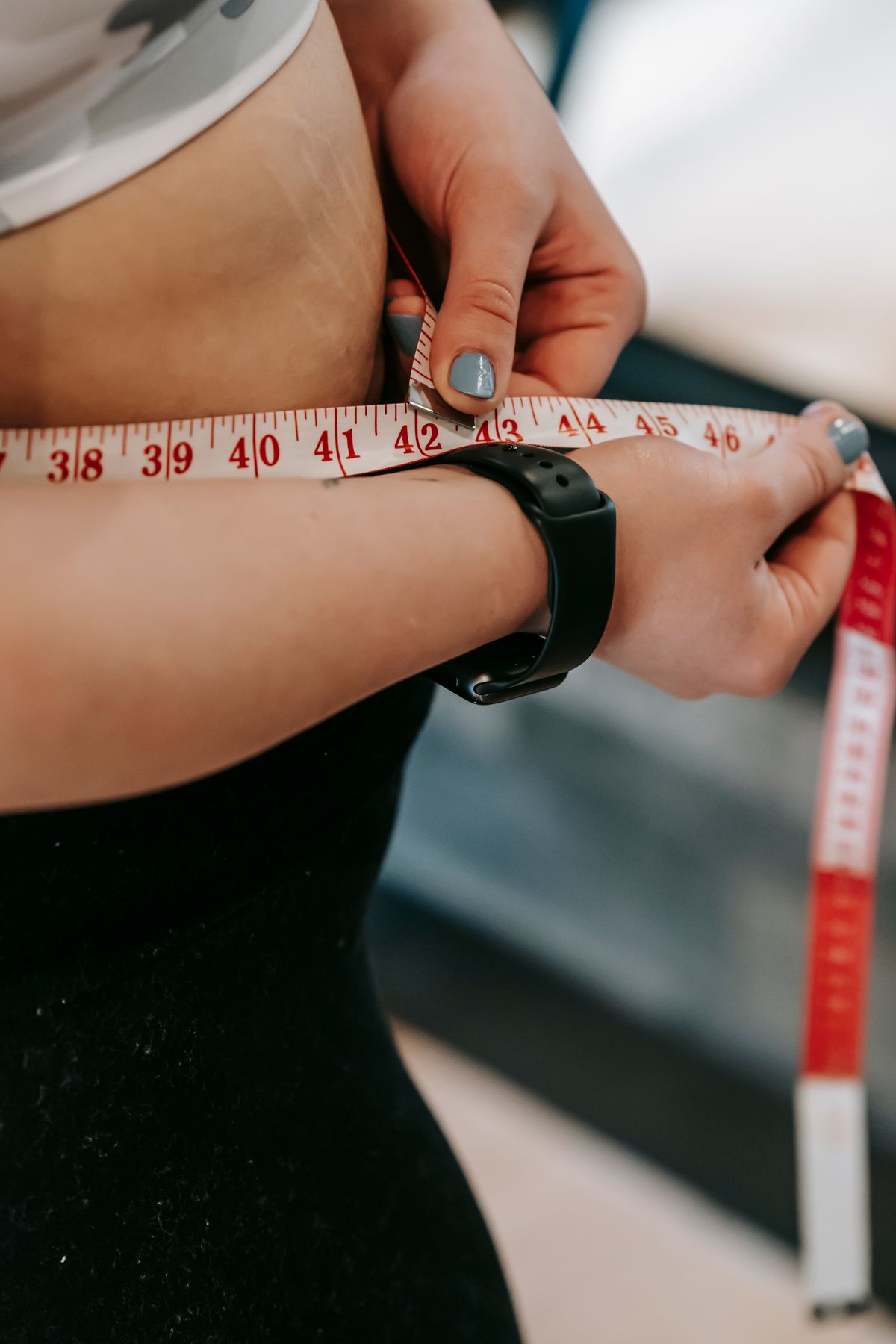 A person measuring their waist with a tape measure, representing a patient on a medical weight loss program
