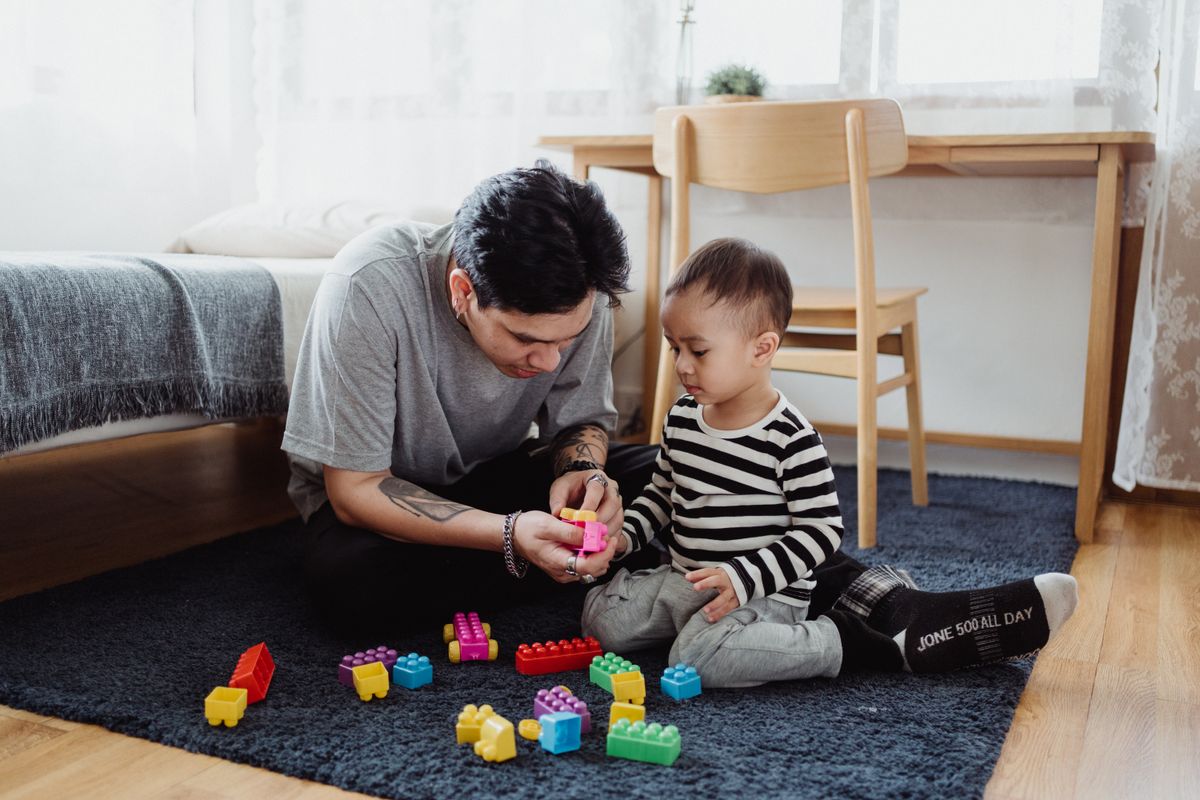 An adult and a young child playing with colorful building blocks on the floor, the everyday work of an ABA therapy session