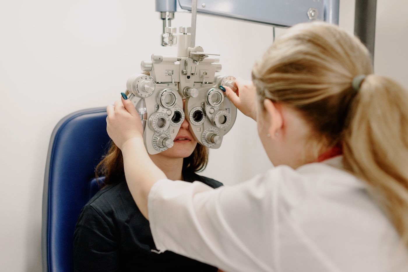 An optometrist using a phoropter during a comprehensive eye exam, representing clinical eye care and optical retail in one practice