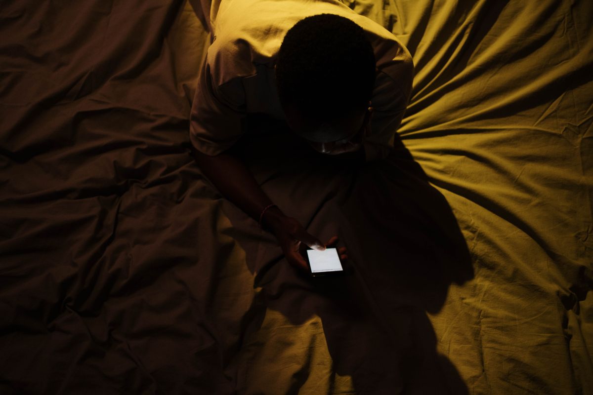 A patient alone in a dark bedroom searching a sensitive health question on a phone late at night
