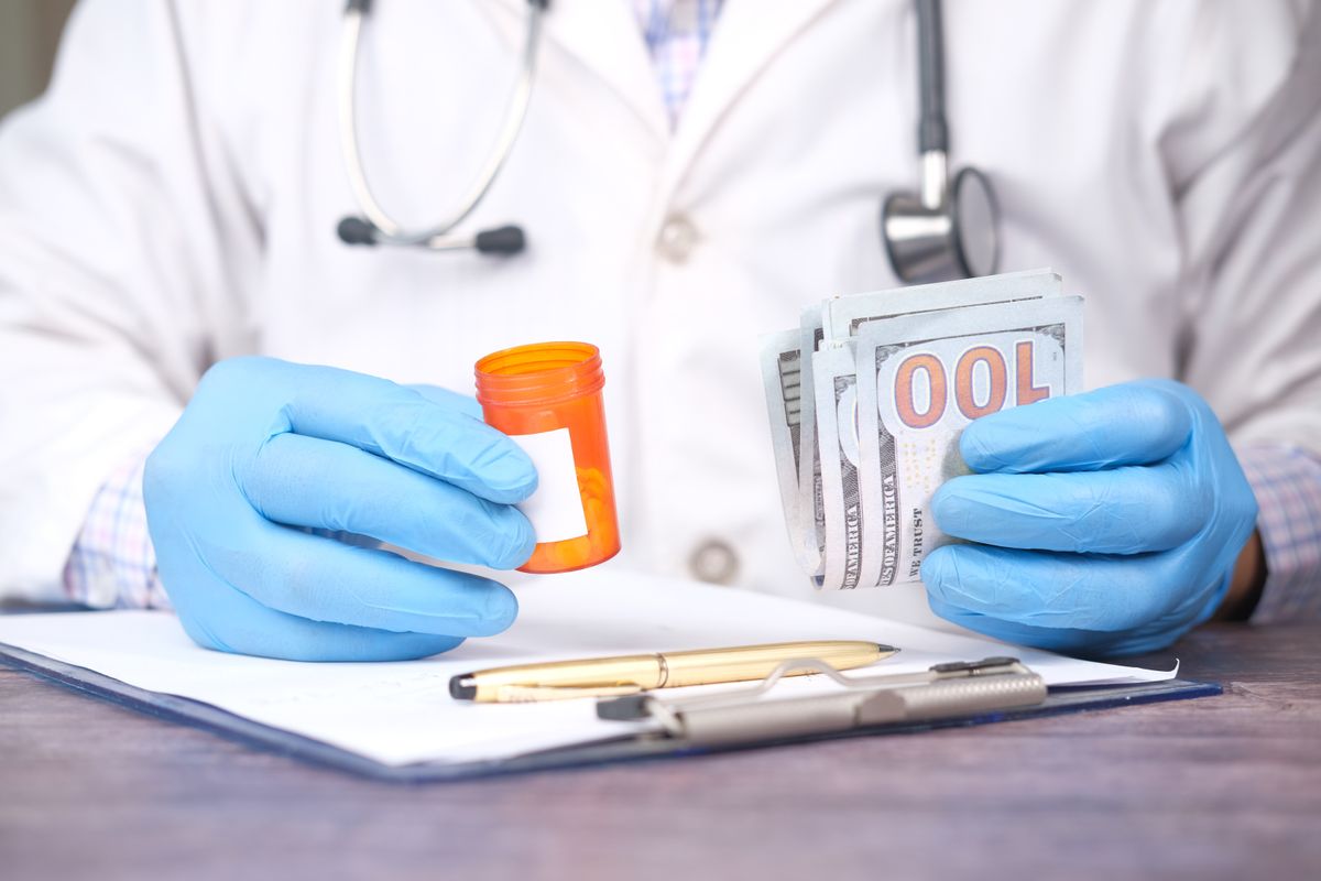 A doctor holding a prescription bottle and cash, showing the cost pressure that makes patients cut back on medical care