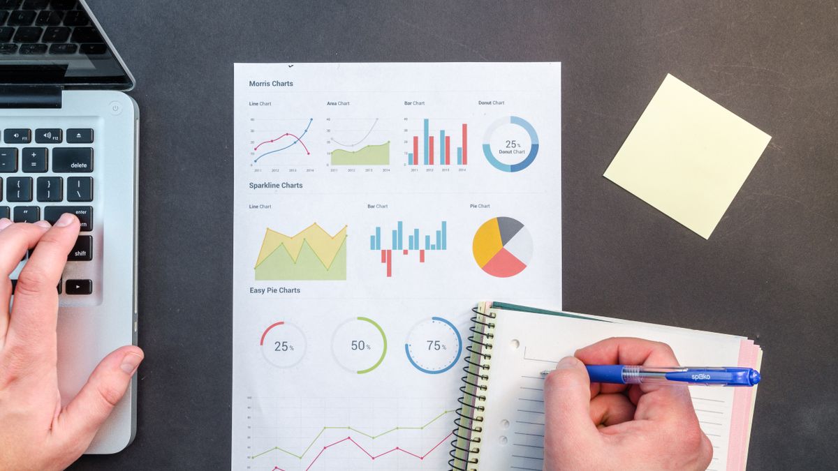 Hand reviewing a printed report full of charts next to a laptop, standing in for reading your Google Business Profile performance report