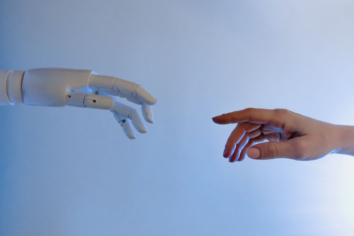 A white robotic hand reaching toward a human hand, representing healthcare AI meeting the patient experience at a medical practice