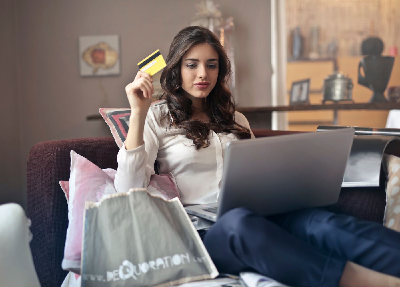 A woman on her couch holding a credit card while looking at a laptop, the moment a patient signs up for or tries to cancel an auto renewing medical practice membership online