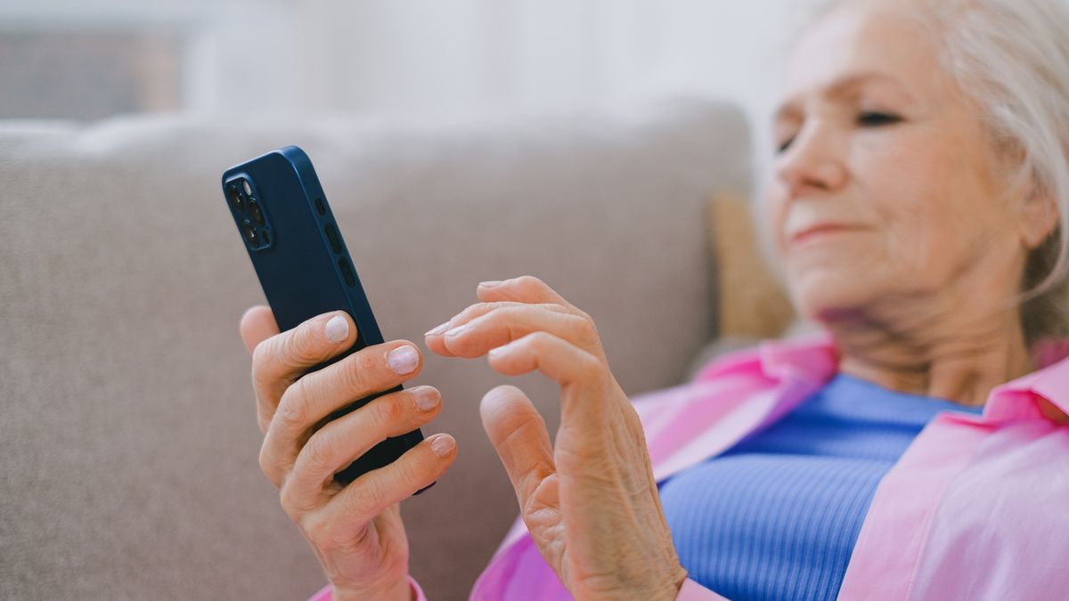 Older patient comfortably using a smartphone at home, showing that seniors text and book appointments online