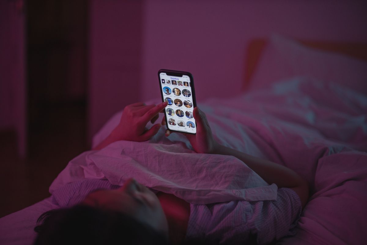 A patient lying in bed at night typing a health question into a smartphone, the screen lighting up the dark room
