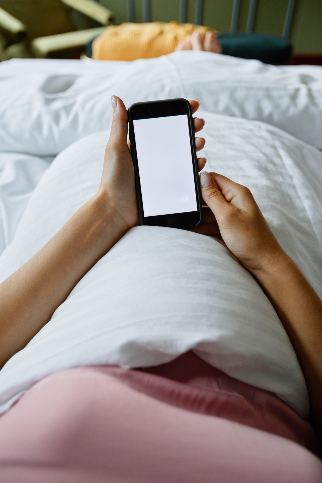 Person in bed at night typing a health question into a phone, the way patients now ask AI whether to see a doctor
