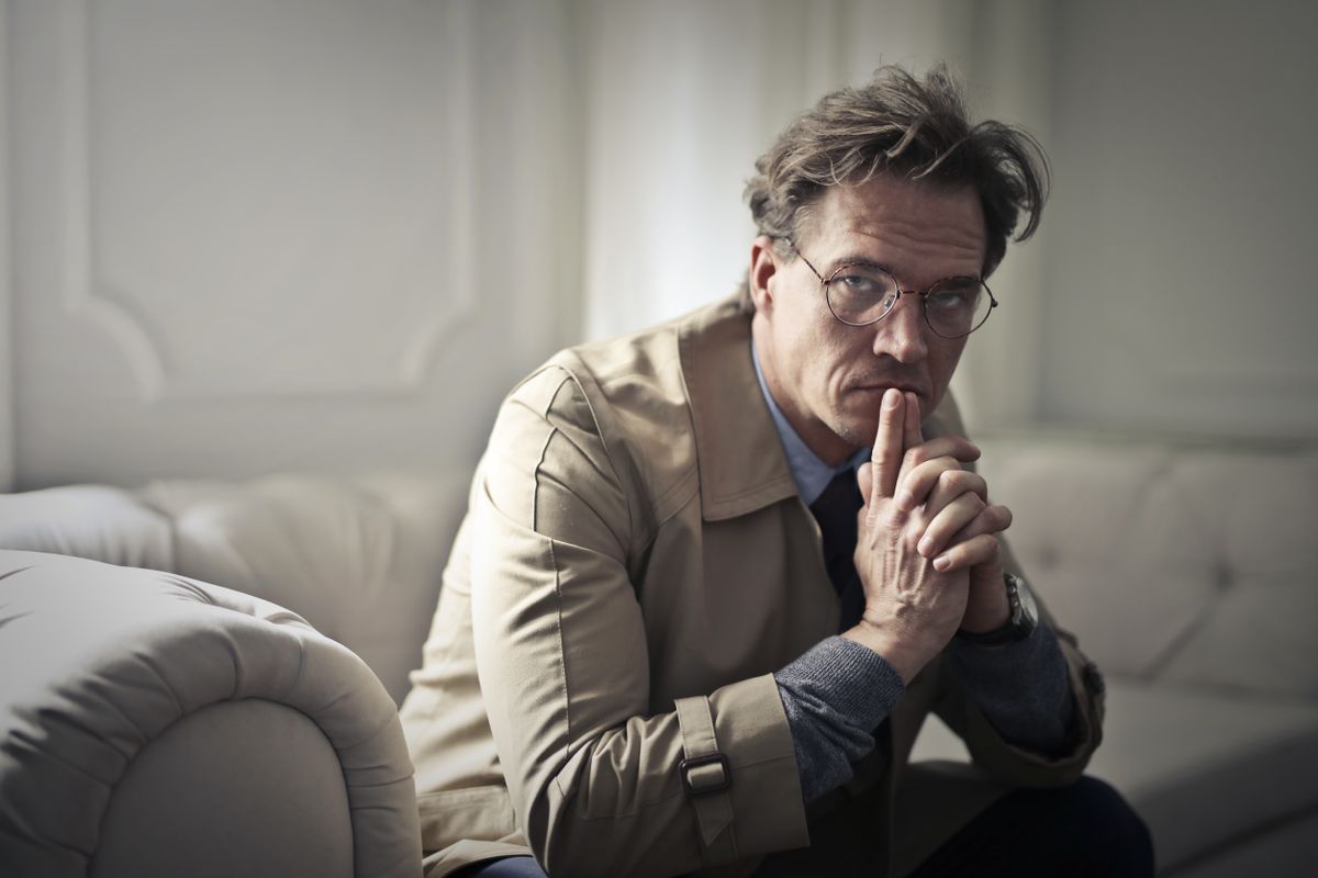 A man sitting on a couch looking uncertain as he reconsiders a medical appointment he already booked after reading online reviews
