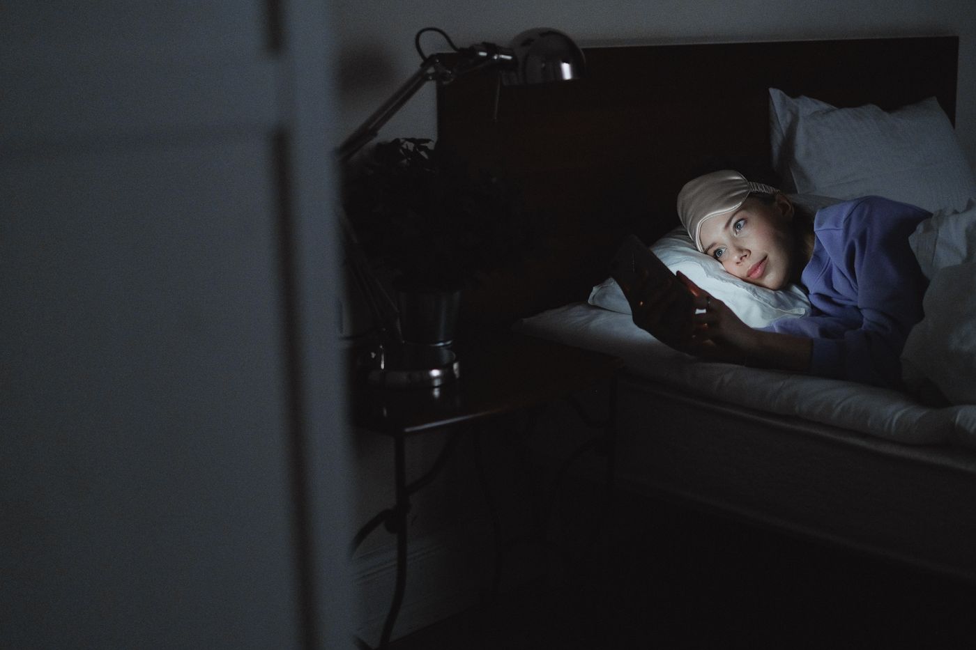 A patient lying in bed at night, face lit by a phone screen, asking AI about their symptoms before booking a doctor