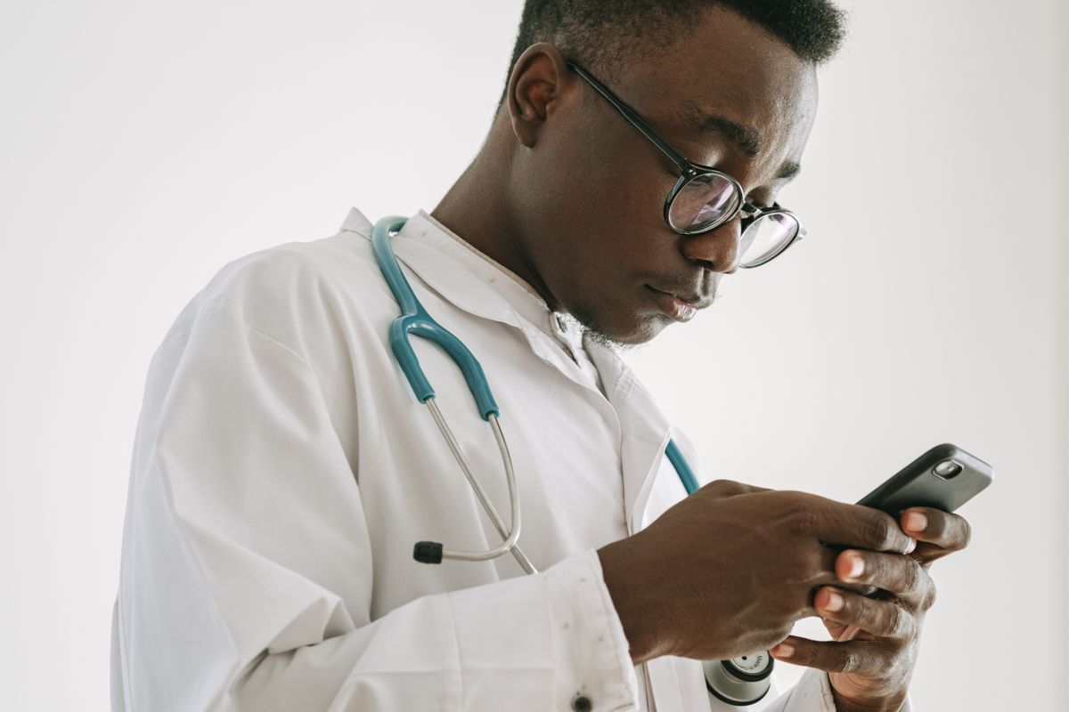 Doctor in a white coat with a stethoscope reading a message on a phone, the human review patients want behind AI patient communication