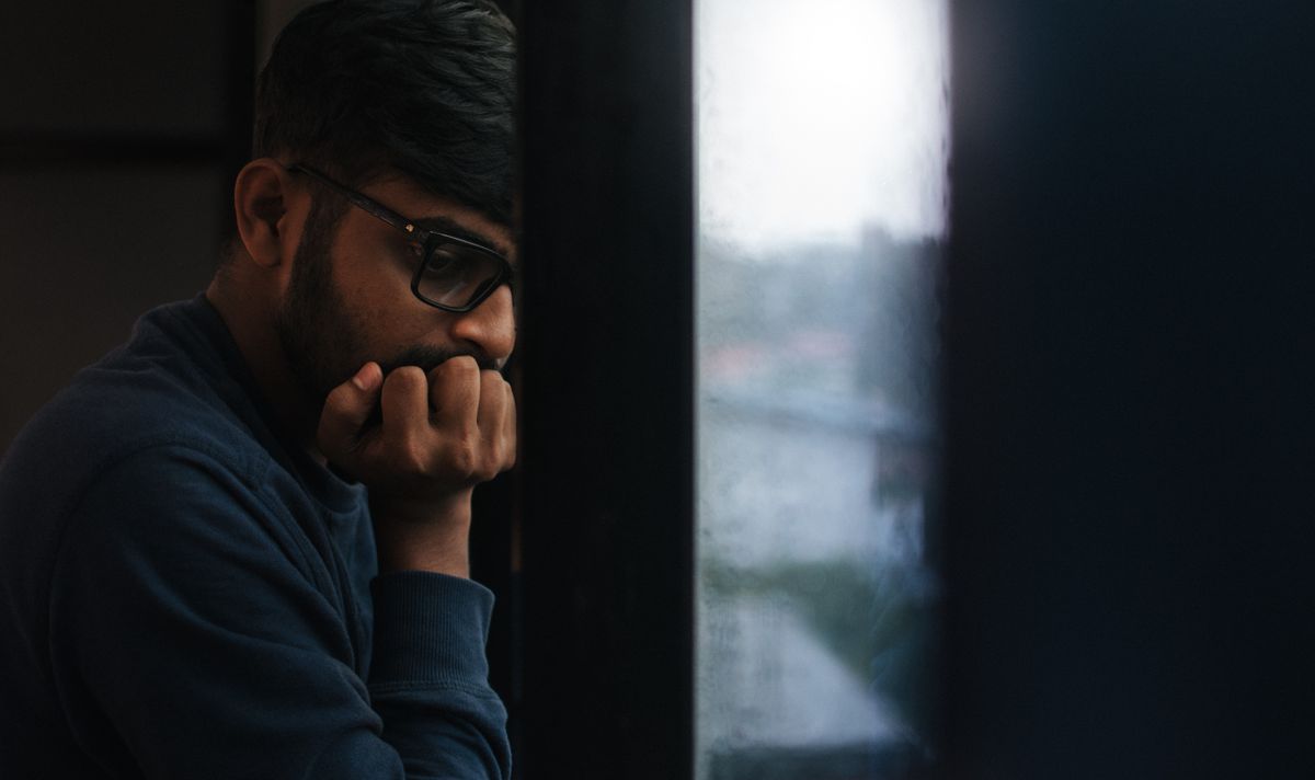 A thoughtful person looking out a rainy window in fall, representing the seasonal rise in people searching for a therapist