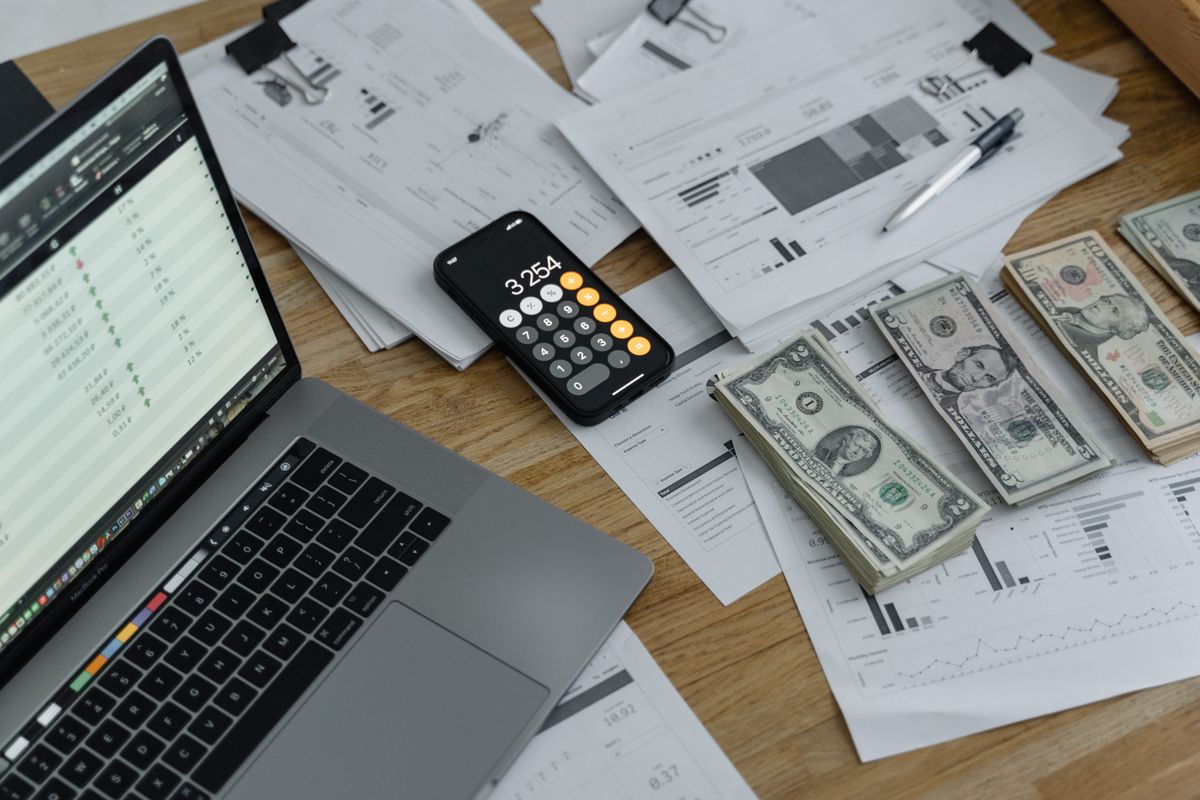 A laptop, a calculator and stacks of cash on a desk covered in spreadsheets, the real math behind whether a new patient discount actually pays off for a medical practice