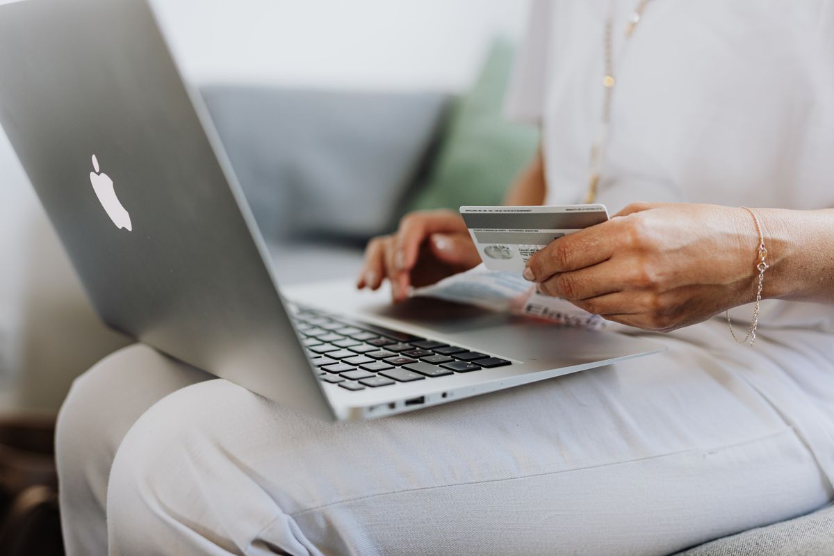 Patient holding a credit card at a laptop, the kind of card on file or deposit a medical practice takes at booking to reduce no shows